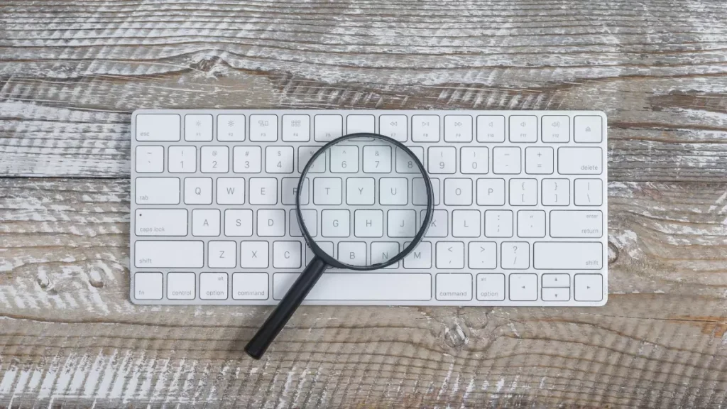 Imagem de um teclado de computador com uma lupa sobre as teclas, simbolizando busca e consulta, relacionada a como consultar precatório 2025.