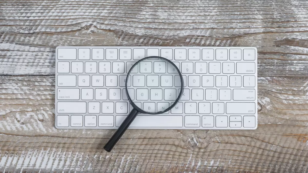 Imagem de um teclado de computador com uma lupa sobre as teclas, simbolizando busca e consulta, relacionada a como consultar precatório 2025.